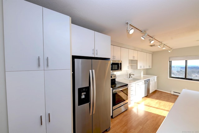 kitchen with appliances with stainless steel finishes, sink, white cabinetry, a baseboard heating unit, and light hardwood / wood-style floors