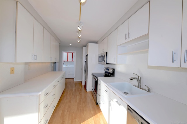 kitchen with washer and dryer, light wood-type flooring, stainless steel appliances, white cabinets, and sink