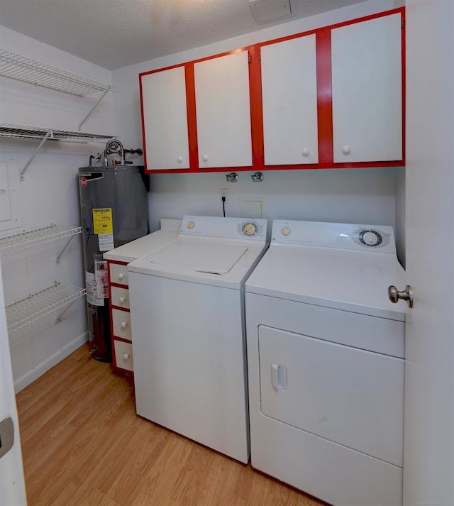 laundry area with cabinets, water heater, washer and clothes dryer, and light hardwood / wood-style floors