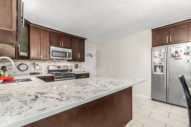 kitchen featuring dark brown cabinetry, sink, light stone countertops, and appliances with stainless steel finishes