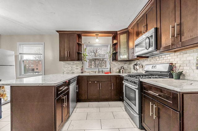 kitchen with sink, backsplash, light stone counters, kitchen peninsula, and stainless steel appliances