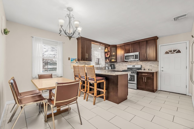 kitchen with tasteful backsplash, decorative light fixtures, dark brown cabinets, and stainless steel appliances