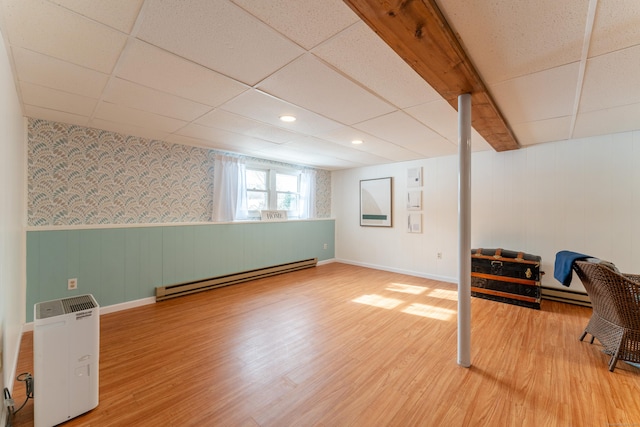 basement featuring hardwood / wood-style flooring, a baseboard heating unit, and a paneled ceiling