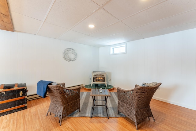 sitting room with a drop ceiling, hardwood / wood-style floors, and a wood stove