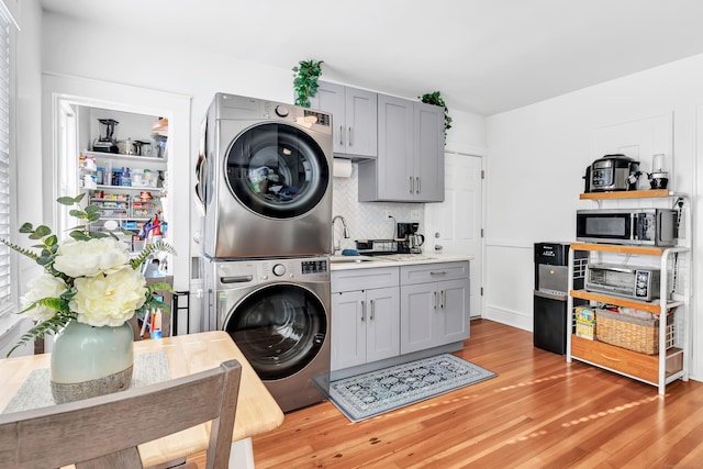 laundry room with stacked washer / drying machine, light hardwood / wood-style flooring, and sink