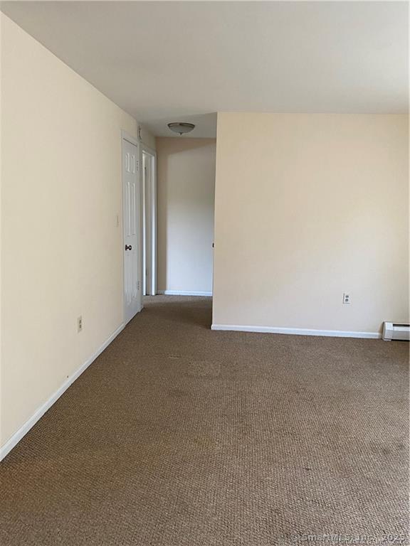 empty room featuring baseboard heating and dark colored carpet