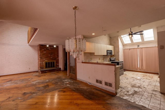 kitchen with a brick fireplace, hanging light fixtures, electric range, ceiling fan, and vaulted ceiling with skylight