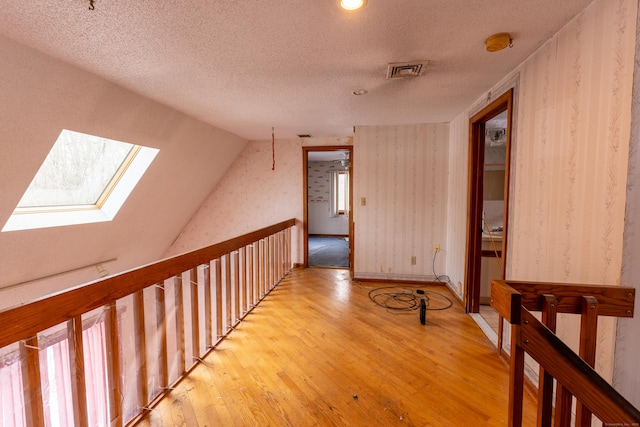 corridor with light hardwood / wood-style flooring, lofted ceiling with skylight, and a textured ceiling