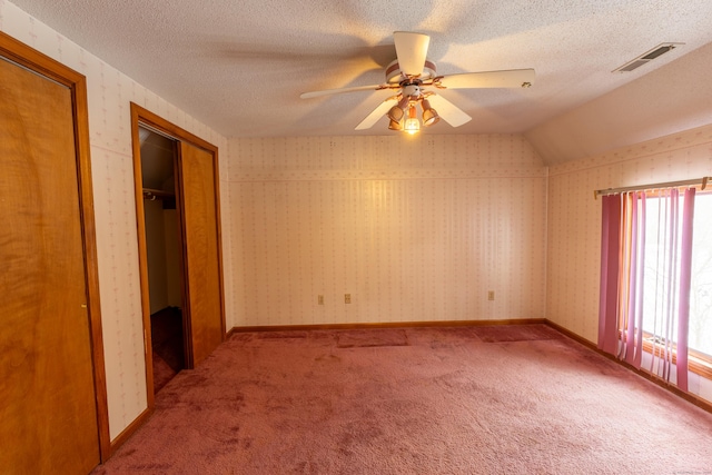 empty room featuring ceiling fan, vaulted ceiling, light colored carpet, and a textured ceiling