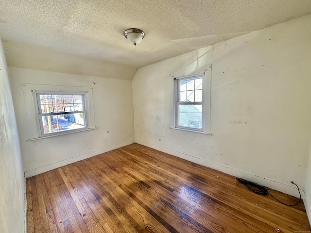 empty room featuring lofted ceiling, hardwood / wood-style floors, a textured ceiling, and a wealth of natural light