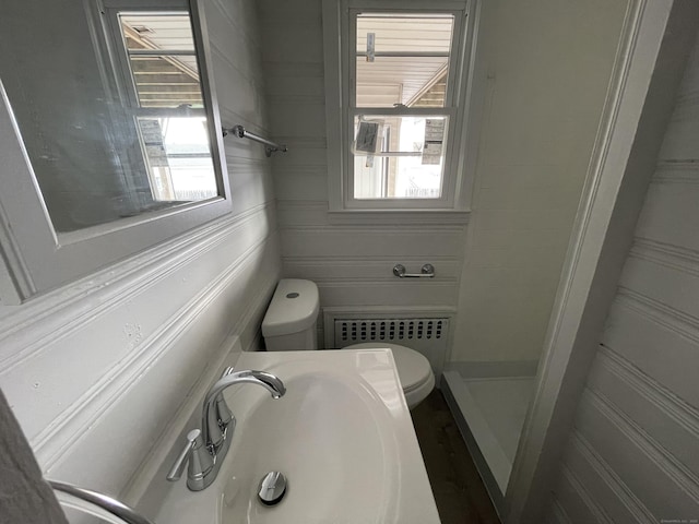 bathroom featuring radiator heating unit, toilet, sink, and a wealth of natural light