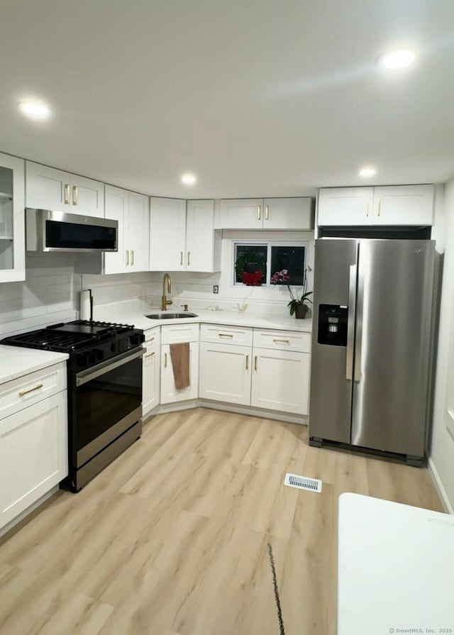 kitchen with sink, stainless steel appliances, tasteful backsplash, light hardwood / wood-style floors, and white cabinets