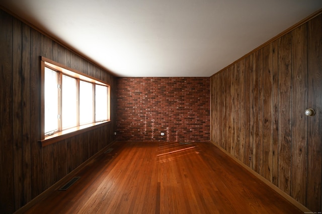 spare room with hardwood / wood-style flooring, brick wall, and wood walls