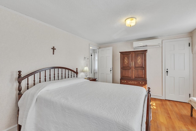 bedroom featuring an AC wall unit, a textured ceiling, and light hardwood / wood-style flooring