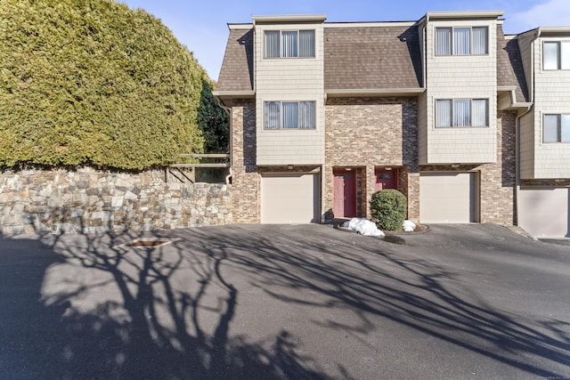 view of property featuring a shingled roof, an attached garage, and brick siding