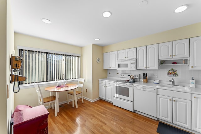 kitchen with light wood finished floors, light countertops, decorative backsplash, a sink, and white appliances