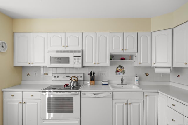 kitchen featuring white appliances, a sink, white cabinets, light countertops, and decorative backsplash