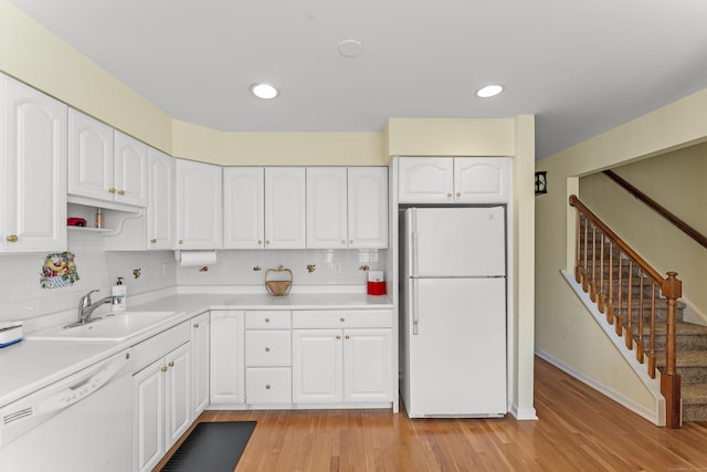 kitchen with light wood finished floors, white appliances, a sink, and white cabinetry