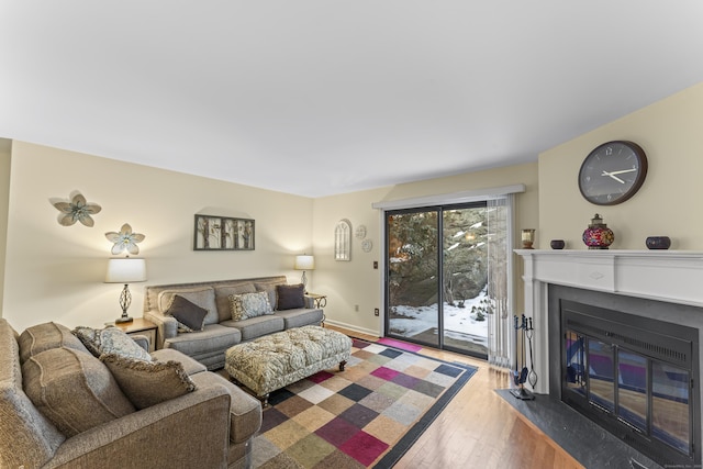 living room featuring a fireplace with flush hearth, baseboards, and wood finished floors