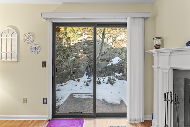 doorway with a fireplace, wood finished floors, a wealth of natural light, and baseboards