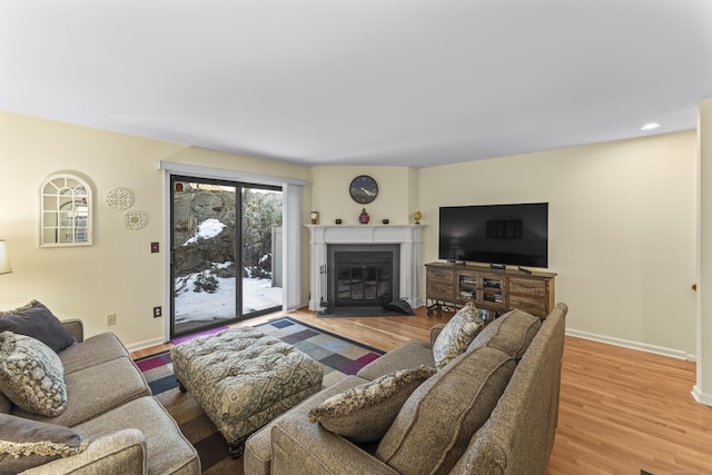 living area with a glass covered fireplace, recessed lighting, baseboards, and wood finished floors