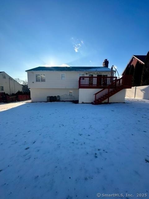 snow covered back of property with a wooden deck