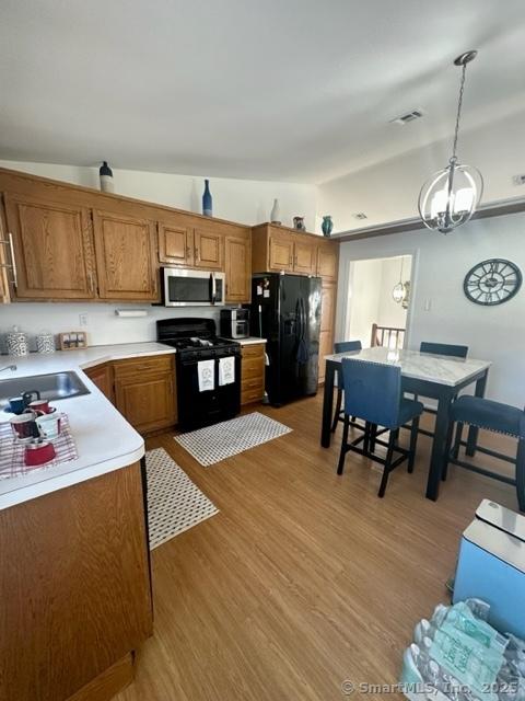 kitchen featuring pendant lighting, sink, light hardwood / wood-style flooring, a notable chandelier, and black appliances