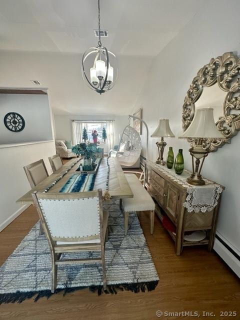 dining space featuring dark wood-type flooring, vaulted ceiling, baseboard heating, and a notable chandelier