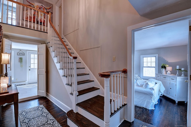 stairway with a towering ceiling, wood-type flooring, and a baseboard heating unit