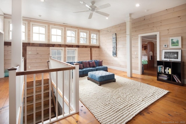 living room featuring wood-type flooring, wooden walls, and ceiling fan