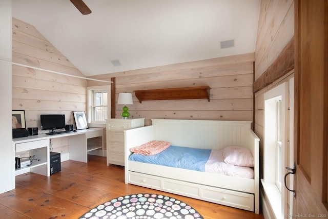 bedroom with hardwood / wood-style floors, vaulted ceiling, and wooden walls