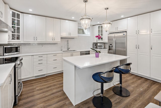 kitchen featuring stainless steel appliances, white cabinetry, light countertops, a center island, and glass insert cabinets