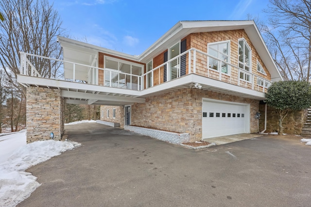 view of front of home featuring aphalt driveway, stone siding, a balcony, and an attached garage