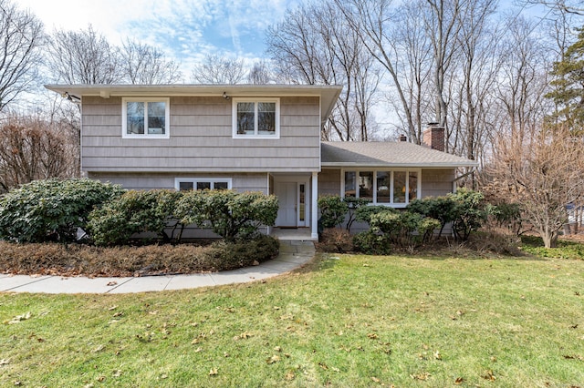 view of front of home featuring a chimney, a front yard, and a shingled roof