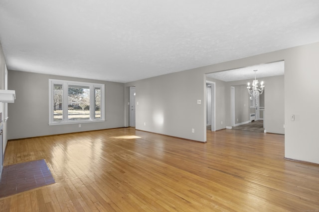 unfurnished living room featuring an inviting chandelier, light hardwood / wood-style floors, and a textured ceiling