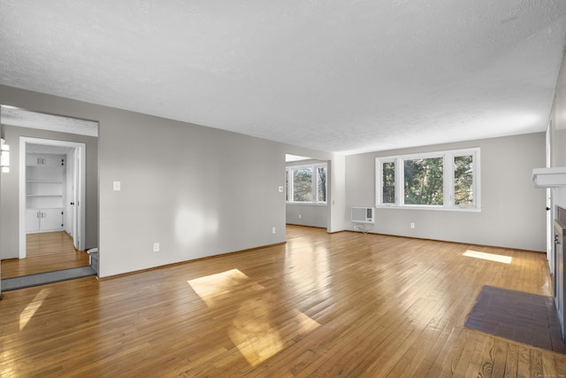 unfurnished living room with heating unit, plenty of natural light, a textured ceiling, and light wood-type flooring