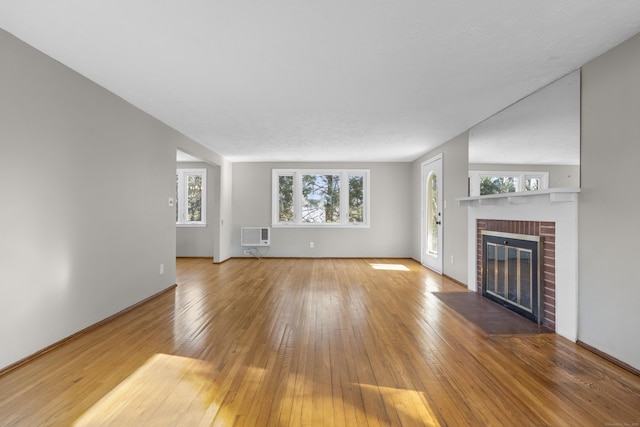 unfurnished living room featuring hardwood / wood-style flooring, a wall mounted AC, and a fireplace