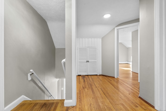 hallway with vaulted ceiling, a baseboard heating unit, and light wood-type flooring