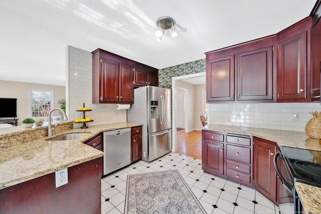 kitchen with sink, stainless steel appliances, light stone counters, tasteful backsplash, and a textured ceiling