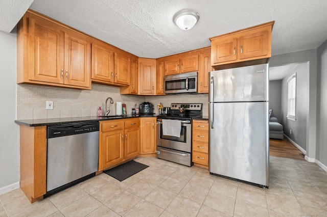 kitchen with stainless steel appliances, a textured ceiling, backsplash, light tile patterned floors, and sink