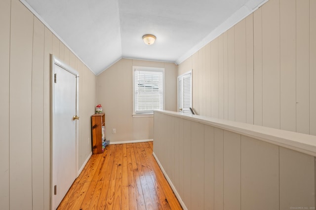 hallway with light wood-type flooring, ornamental molding, and lofted ceiling