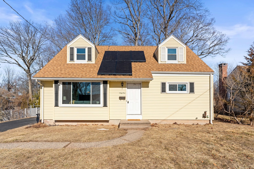 cape cod house featuring a front lawn and solar panels