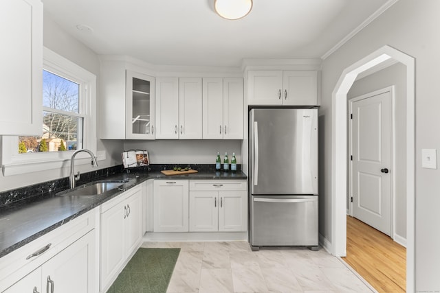 kitchen with white cabinetry, sink, stainless steel refrigerator, and dark stone countertops