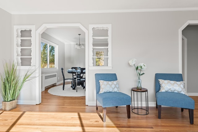 living area with hardwood / wood-style flooring, ornamental molding, radiator, and an inviting chandelier