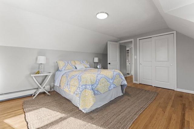 bedroom featuring hardwood / wood-style flooring, lofted ceiling, baseboard heating, and a closet