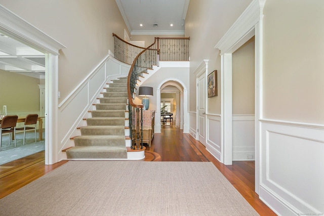 foyer with arched walkways, a decorative wall, stairs, and wood finished floors