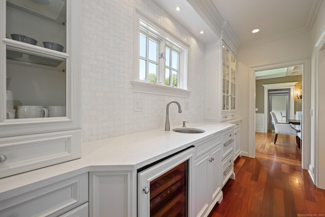 bar featuring beverage cooler, dark wood finished floors, a sink, crown molding, and tasteful backsplash