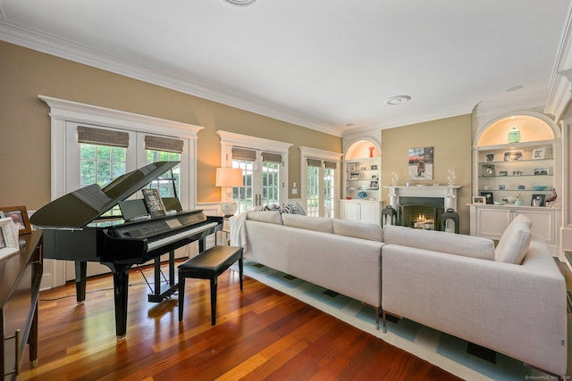 living area featuring built in shelves, a warm lit fireplace, wood finished floors, french doors, and crown molding