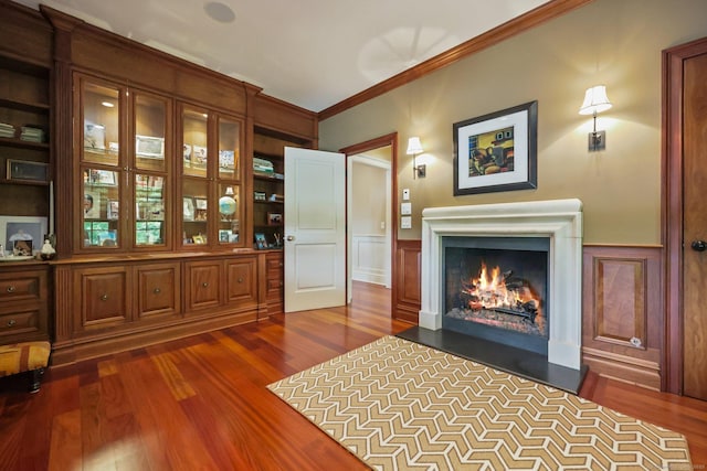 interior space featuring a wainscoted wall, a fireplace with flush hearth, dark wood-type flooring, crown molding, and a decorative wall