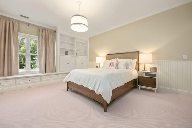 bedroom featuring a wainscoted wall, crown molding, light colored carpet, and visible vents